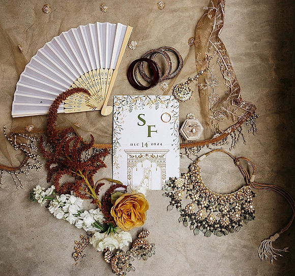 Invitation suite wedding invitation flat lay styled with engagement ring, jewelry, floral sprigs and a rose bloom on a neutral fabric backdrop