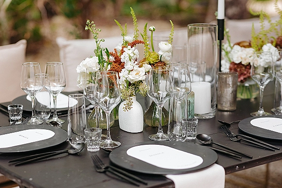 Reception tablescape with modern wedding tablescape styling, black plates and flatware, bud vase florals, and taper candles on a stone patio garden table