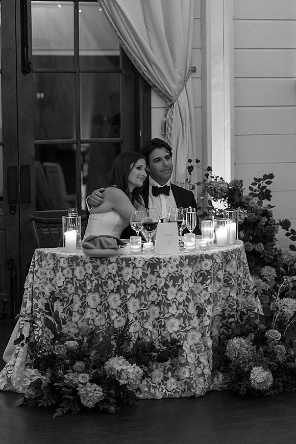 Sweetheart table moment with bride and groom at sweetheart table, candlelit lace tablescape with florals in an indoor reception space