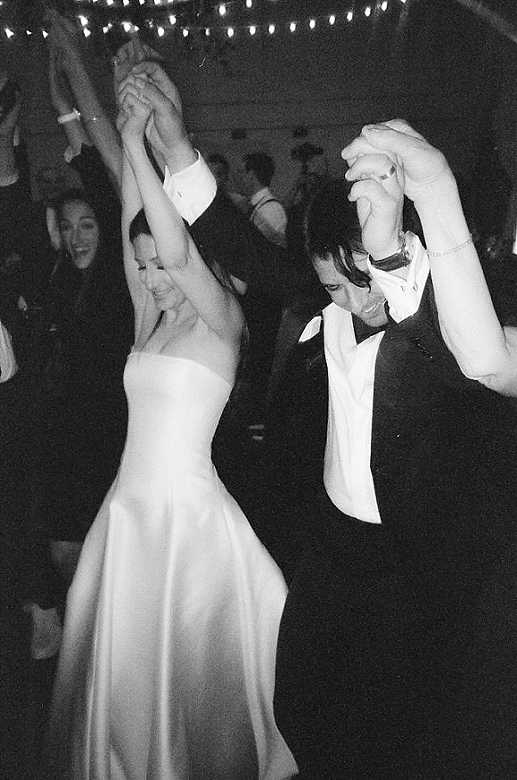 Wedding reception dancing with bride and groom dancing in a dark room, guests raising hands on the dance floor under string lights