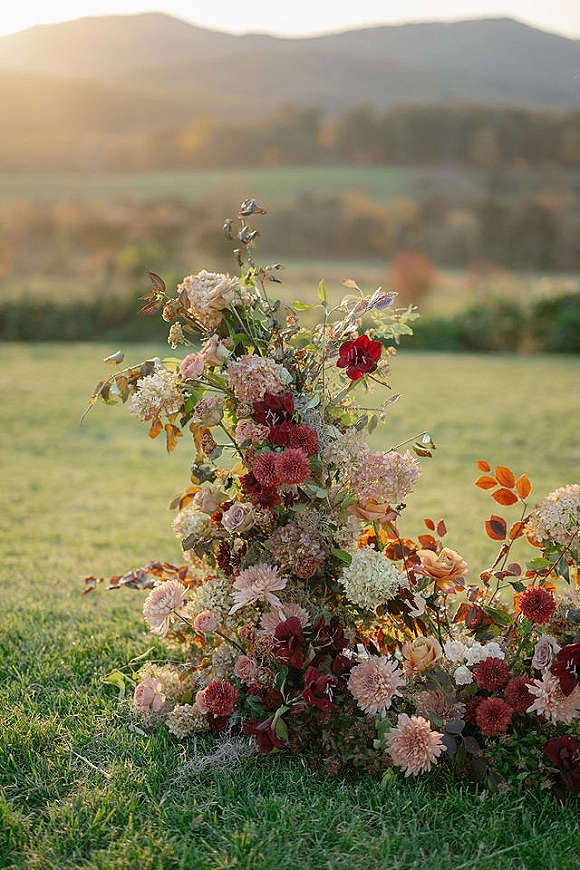 Wedding floral arrangement with ceremony ground florals of roses, dahlias, and hydrangea on a grass lawn with mountains beyond