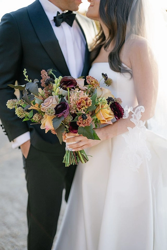 Wedding couple portrait with bride and groom close up, holding a bridal bouquet as she wears a veil beside him in a tux on an outdoor walkway