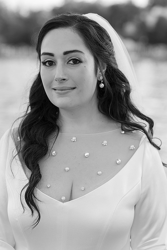Bridal portrait in black and white of a bride with veil and pearl drop earrings, wearing a long sleeve illusion neckline gown outdoors