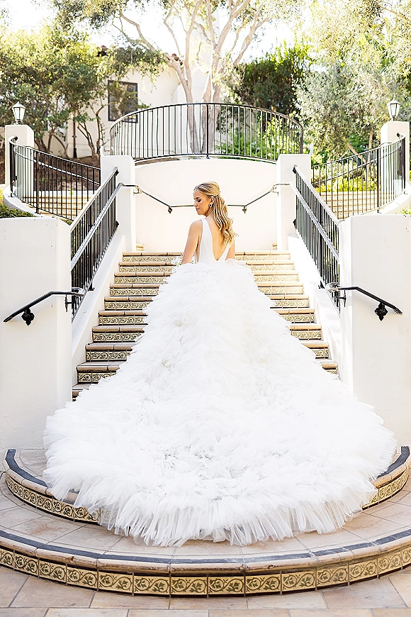 Bridal portrait of a bride in a backless wedding dress with a sweeping tulle train on tiled outdoor steps beside white stucco walls