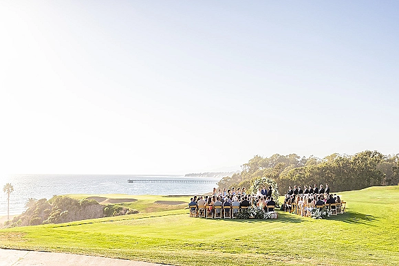 Outdoor wedding ceremony with an ocean view wedding ceremony setup, white floral arch and aisle florals on a grassy lawn by the pier