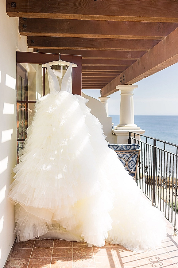 Wedding dress tulle ball gown on a hanger, with layered skirt and deep V neckline on a balcony overlooking the ocean and blue sky