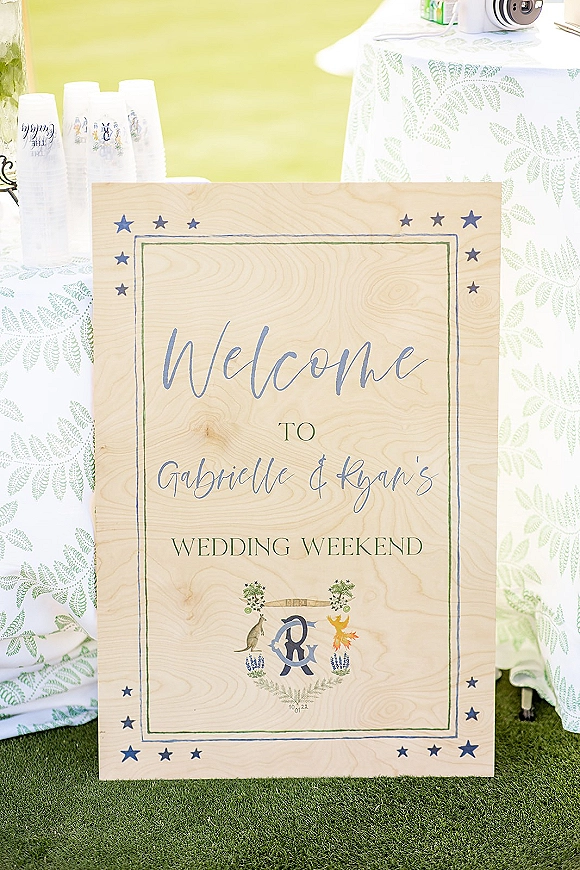 Wedding welcome sign with calligraphy welcome sign lettering, star border, monogram crest and illustrated animals on a lawn table with cups