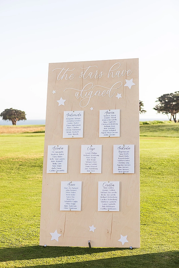 Wedding seating chart celestial seating chart on a wood board with calligraphy, clipped cards and paper stars on a coastal lawn backdrop