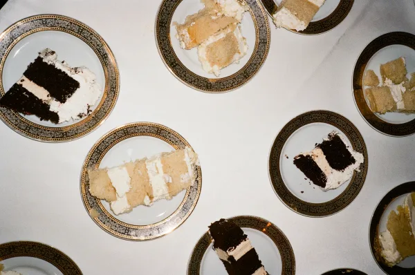 Wedding cake slices on gold rim china plates with buttercream frosting arranged on a white tablecloth for a reception dessert table