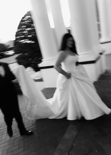 Wedding exit moment in a black and white wedding photo as bride runs holding her train beside groom along brick walkway past white columns