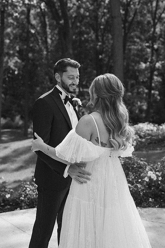 Couple portrait in a black and white wedding portrait, bride in off-shoulder dress and groom in tuxedo embracing on a garden path