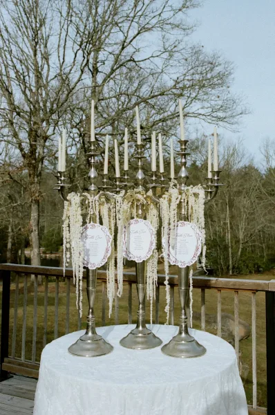 Wedding seating chart with silver candelabra seating chart display, taper candles, and hanging white florals on a deck overlooking trees