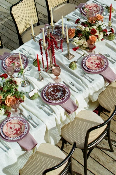 Reception tablescape with lavender napkins, patterned plates, pink goblets, and silver candelabras with taper candles on a wood deck