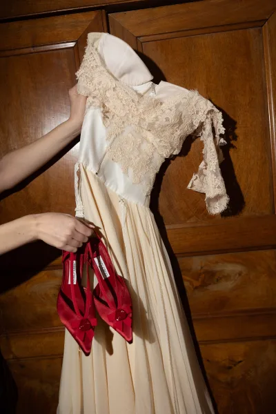 Wedding dress with lace sleeve details and high neckline, showing satin pleated skirt and red bow heels against a wood paneled wall