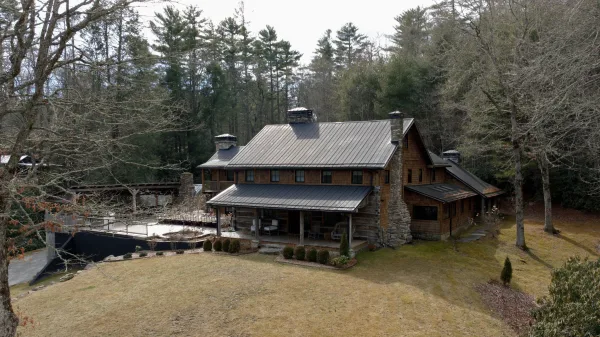Rustic wedding venue, mountain wedding venue wood cabin with stone chimney and metal roof, covered porch and deck set by forest trees