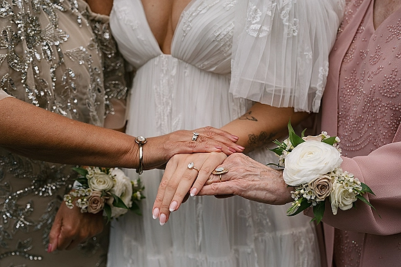 Wedding ring photo of bridal party hands stacked, showing engagement ring close up, manicured nails, and rose corsage over dresses