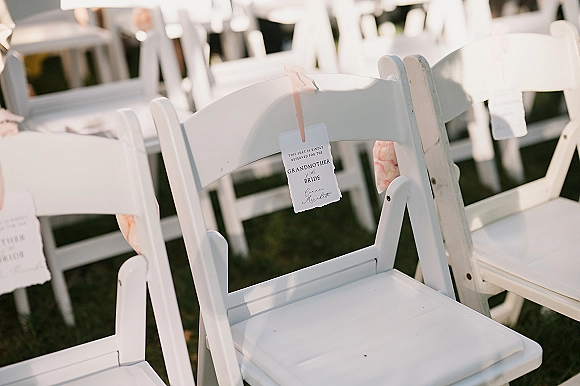 Ceremony reserved seating with a reserved seat sign tied by ribbon to white folding chairs in neat rows on a grass lawn outdoors