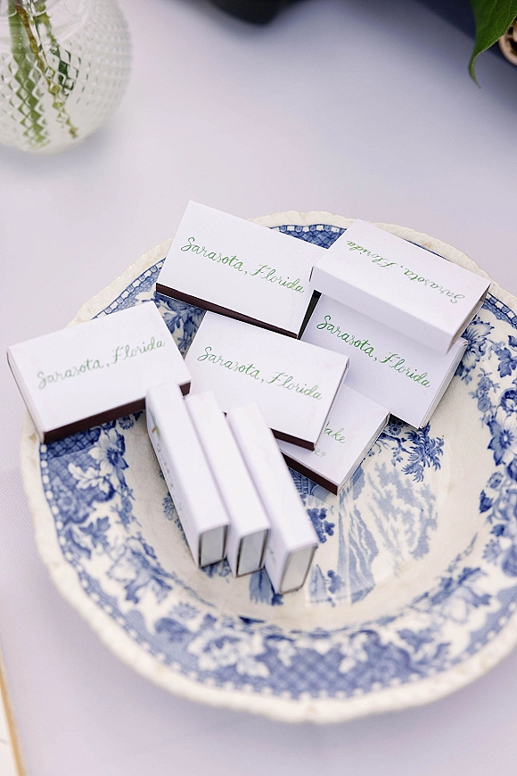 Wedding matchboxes with personalized matchboxes wedding favor in green calligraphy on a blue and white china plate atop a white tablecloth