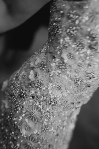 Wedding dress close-up showing a beaded wedding dress bodice with intricate floral appliqué and shimmer, set against a softly blurred indoor background