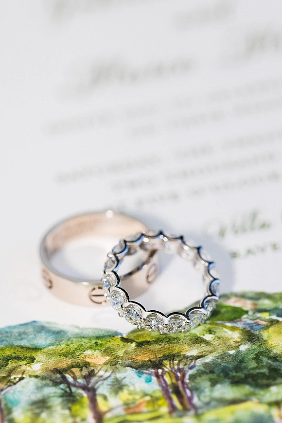 Wedding rings in a wedding ring flat lay, featuring a diamond eternity band and engraved gold band on white paper with blurred calligraphy