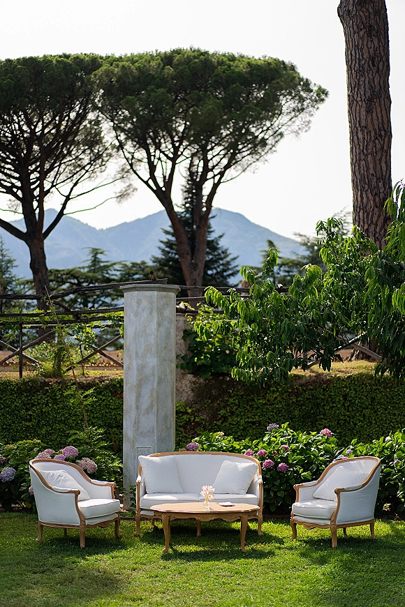 Wedding lounge area with outdoor sofa and upholstered armchairs around a coffee table, set on a lawn with mountains beyond