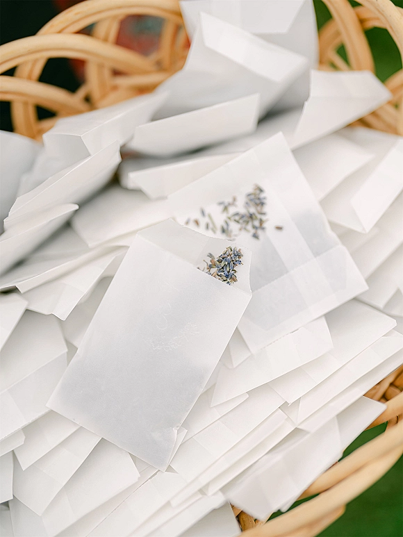 Wedding confetti bags with lavender confetti tucked in a wicker basket on green grass, ready for a ceremony exit toss