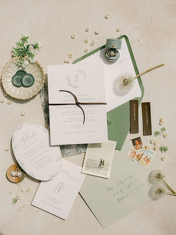 Invitation suite wedding invitation flat lay with sage green envelopes, wax seals, silk ribbon, rings and pearl earrings on neutral linen