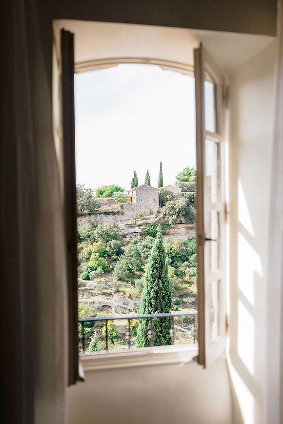 Bridal suite window with open shutters, framing a balcony railing and hillside landscape of trees, stone buildings, and sky