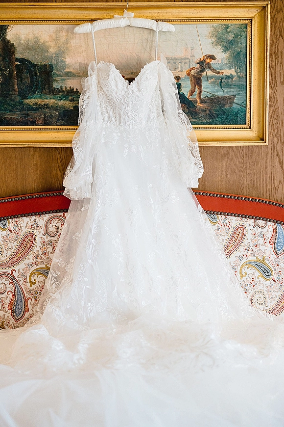Wedding dress with lace wedding dress bodice, sweetheart neckline and tulle skirt hanging on a hanger against a wood-paneled wall