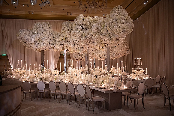 Reception tablescape with white wedding tablescape florals, candlelit glass holders, and hanging flower canopy beneath chandeliers in a draped ballroom