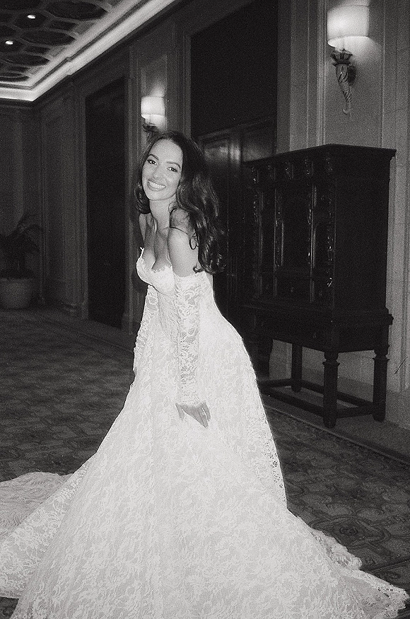 Bridal portrait in a black and white bridal photo of a bride in a strapless lace wedding dress, smiling in a hotel hallway with wall sconces
