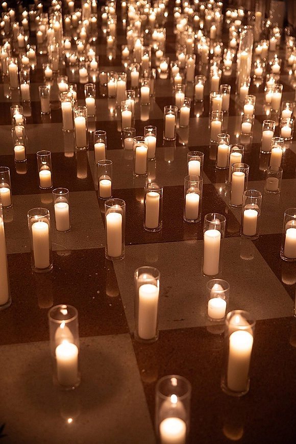 Candlelit aisle decor with wedding aisle candles in glass cylinder vases and pillar candles glowing on a reflective floor in warm light