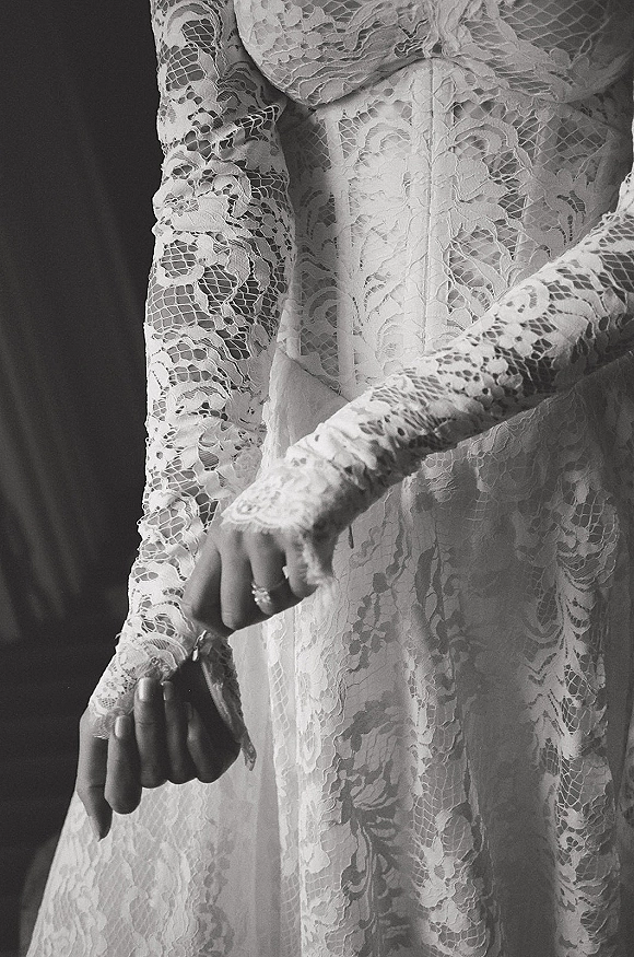 Wedding dress details with lace wedding dress long sleeves and corset bodice, ringed hands near button back against a dark wall