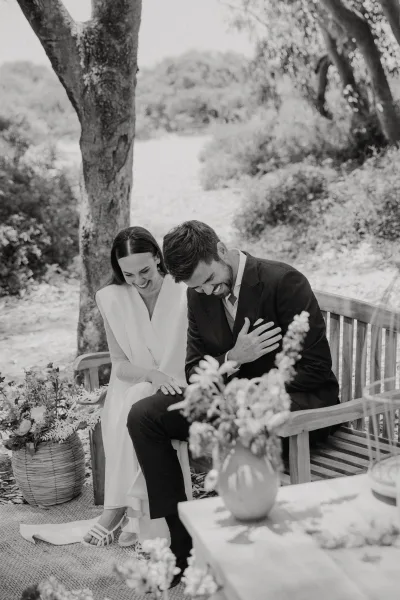 Couple portrait, black and white wedding portrait of bride and groom laughing on a wooden bench in a garden with floral basket accents