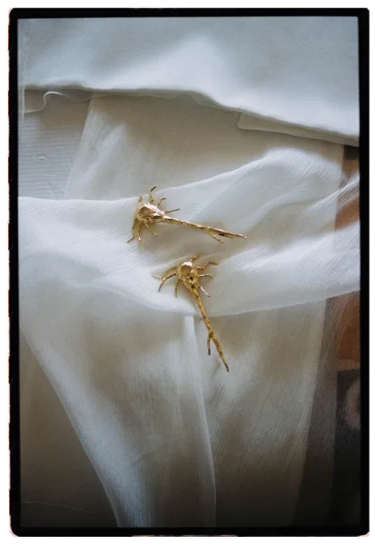 Bridal earrings, gold statement earrings in organic drop shape resting on sheer fabric over a white textile backdrop flatlay