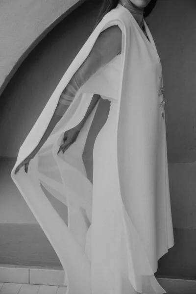 Bridal cape with sheer tulle draping over an embellished bodice, flowing down the staircase beside a textured wall and tiled floor