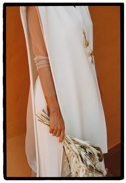 Bridal portrait of a bride in a wedding dress side view, veil draped over her arm, holding a bouquet against a terracotta wall backdrop