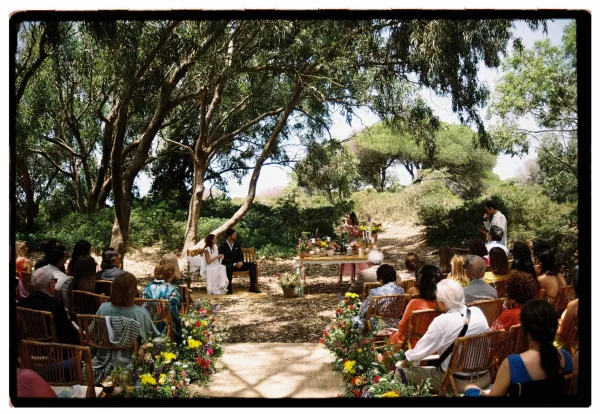 Outdoor wedding ceremony with woodland wedding ceremony seating in the round, wildflower aisle florals, and candlelit table under trees