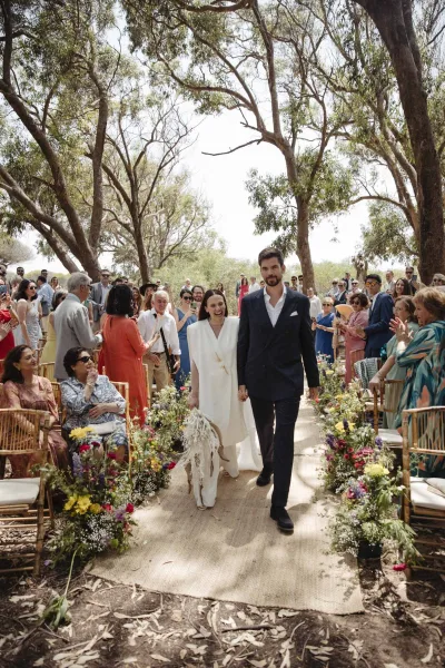 Wedding recessional as bride and groom walk the aisle, bouquet in hand, past colorful wildflower arrangements and cheering guests in a garden setting