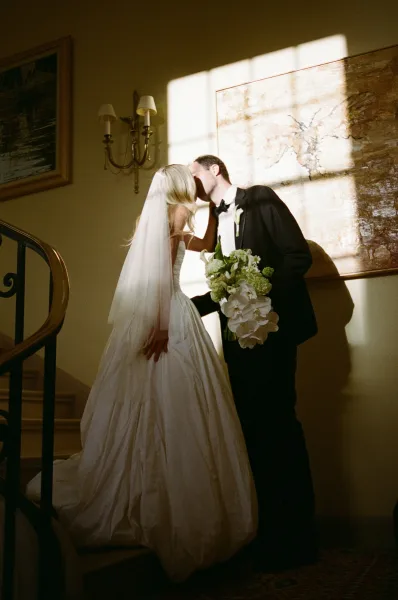 Wedding kiss portrait of newlyweds on a staircase, an indoor wedding portrait with the bride holding a white orchid bridal bouquet.
