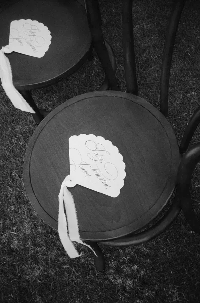 Wedding program fan serving as the ceremony program, tied with a ribbon, resting on a bentwood chair at the ceremony seating