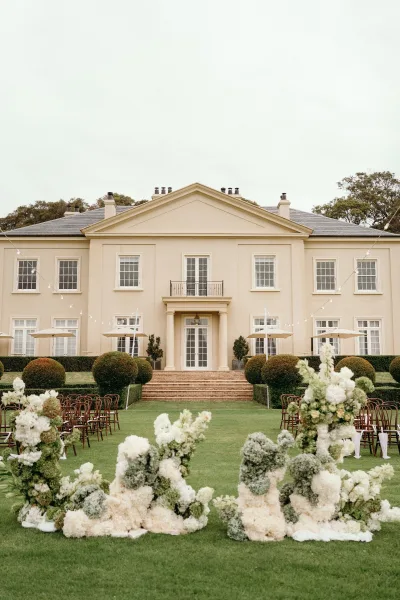 Ceremony setup highlighting ceremony aisle design with bentwood chairs on a lawn facing a mansion facade and stone steps.