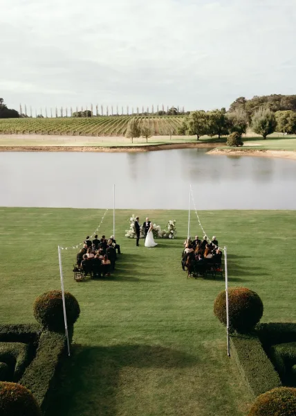 Outdoor ceremony setup with lakeside ceremony decor and white florals framing the aisle, backed by a vineyard, lake, and cloudy sky.