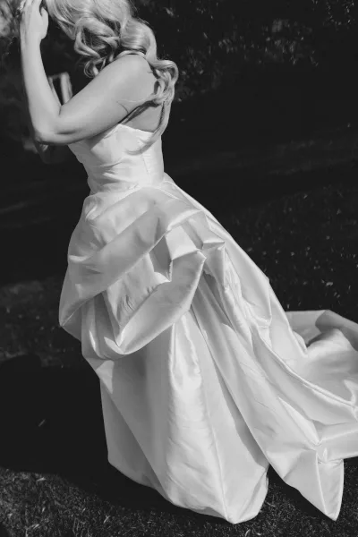 Wedding dress strapless wedding dress in satin with a full skirt and subtle ruching, shown from the side against outdoor greenery