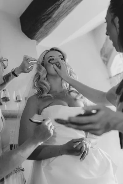 Bridal makeup as a wedding makeup artist applies finishing touches to a veiled bride in a strapless dress, brushes and palette nearby
