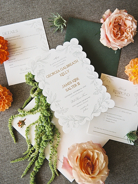Invitation suite with a scalloped wedding invitation, envelope, RSVP and details cards, floral line art, on a linen fabric backdrop