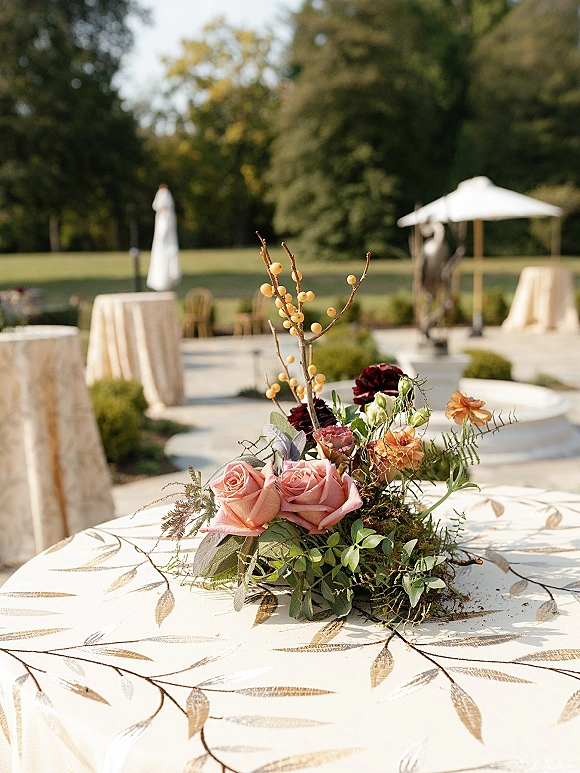 Wedding centerpiece with blush roses and dark red blooms in a garden wedding centerpiece display on a round patio table under an umbrella