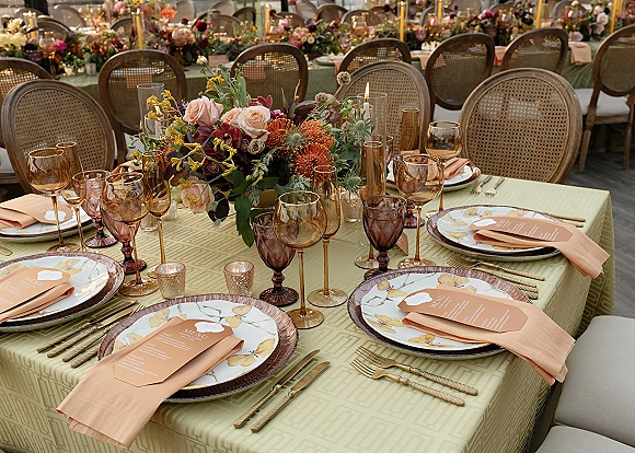 Reception tablescape with wedding reception place setting, floral centerpiece, taper candles, amber and purple goblets, and gold flatware on long tables