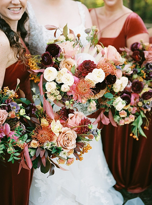 Bridesmaid bouquets in a fall wedding bouquet style with roses, ranunculus, dahlias and eucalyptus, tied with ribbon in outdoor greenery