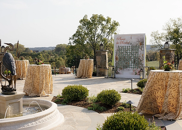 Wedding cocktail hour with outdoor cocktail hour setup featuring patterned linens, floral centerpieces, and a fountain on a stone patio